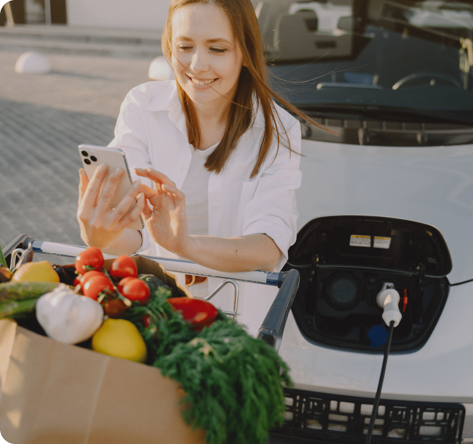 A girl carrying groceries while using her mobile phone outside a modern rental building