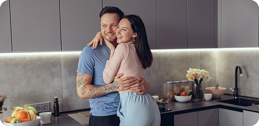 A happy young Caucasian couple embraces in a cozy kitchen, radiating warmth and love in their romantic moment